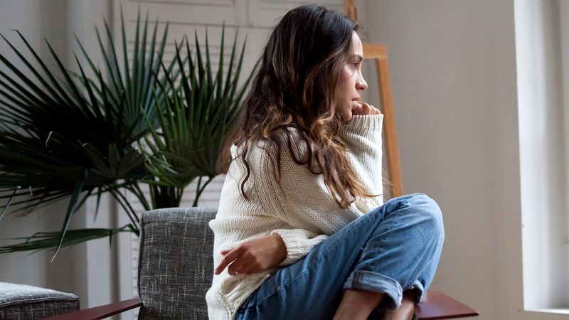 Jeune femme pensive assise chez elle