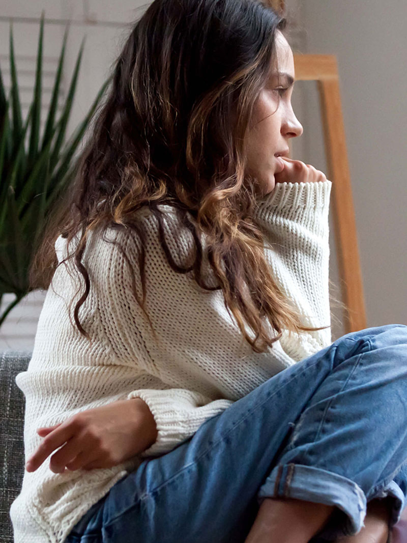 Adolescente con problemas de salud mental sentada en una silla y mirando por una ventana.